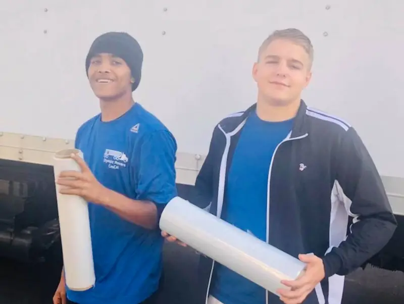Two smiling Olympic crew members holding rolls of protective wrap