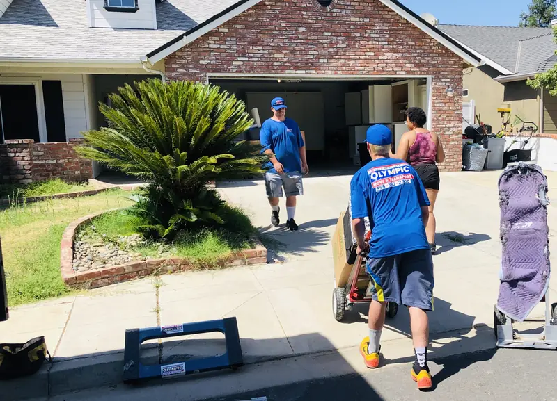Olympic movers with dollies and furniture pads working in a home driveway
