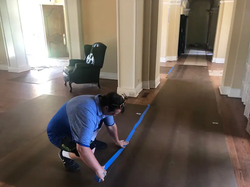 A mover taping down floor protection on hardwood floors before moving furniture