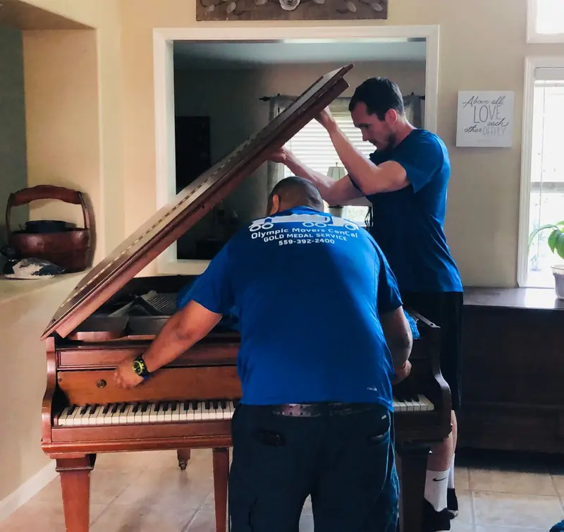 Movers carefully lowering a grand piano onto a piano board