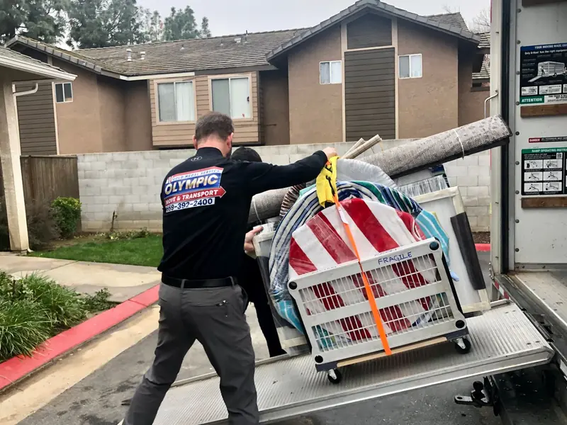 Mover guiding a heavy strapped item on a dolly down a truck ramp