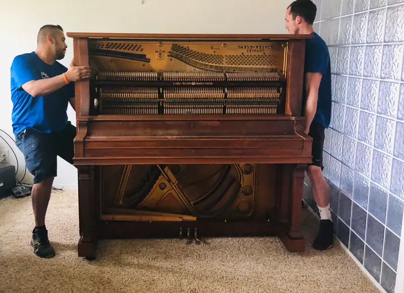 Two movers positioning an antique upright piano
