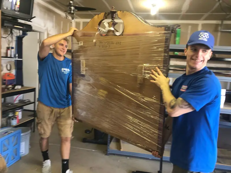 Two movers loading shrink-wrapped furniture into a moving truck